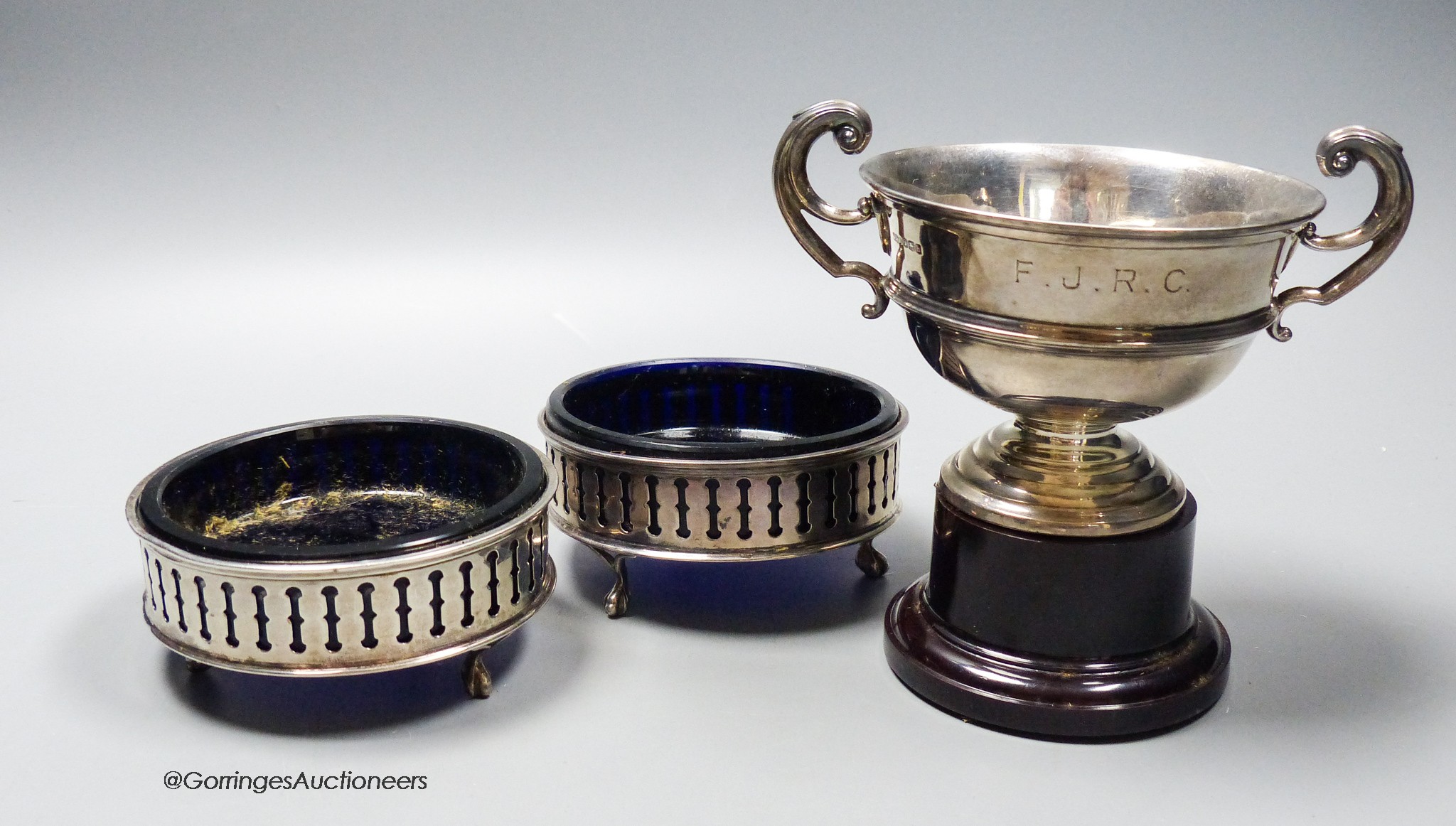 A pair of George V pieced silver small circular dishes with blue glass liners, 10cm and a silver trophy cup on stand, 6.5oz.